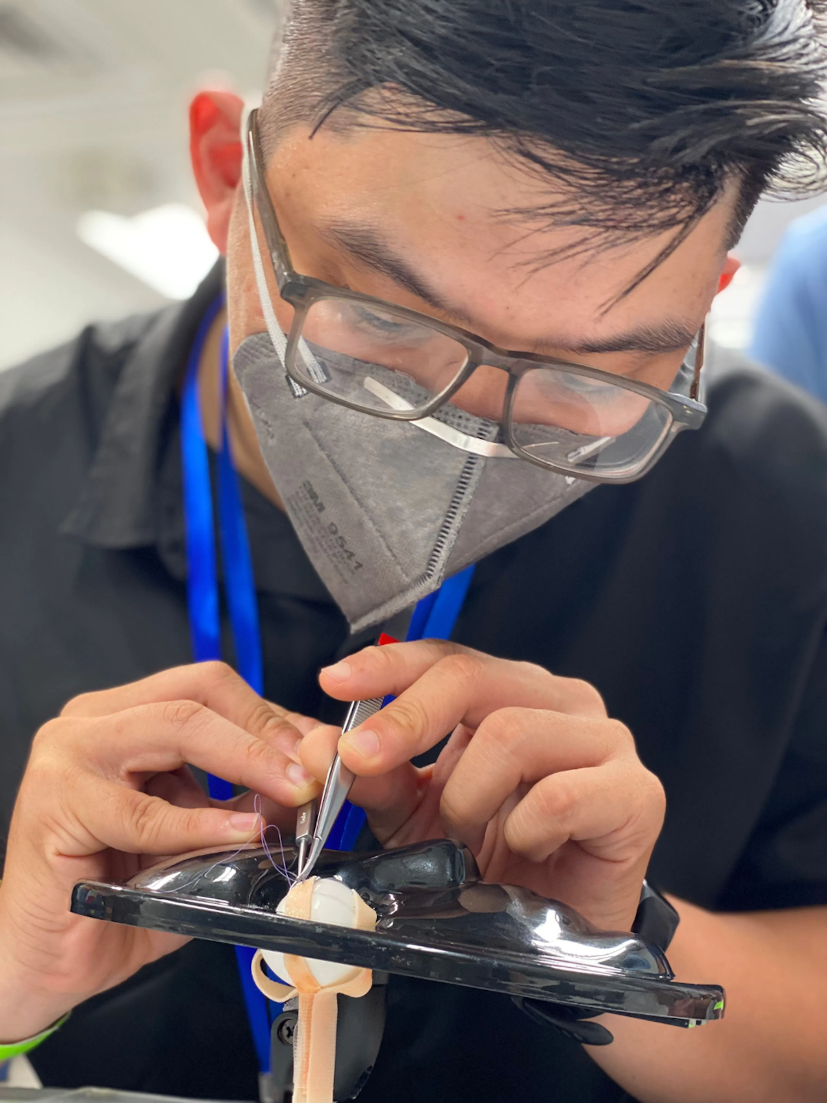 A doctor in glasses and a respiratory mask is practicing strabismus surgery skills on an artificial eye in Can Tho, Vietnam on board the Orbis Flying Eye Hospital. (Image courtesy of Orbis International)