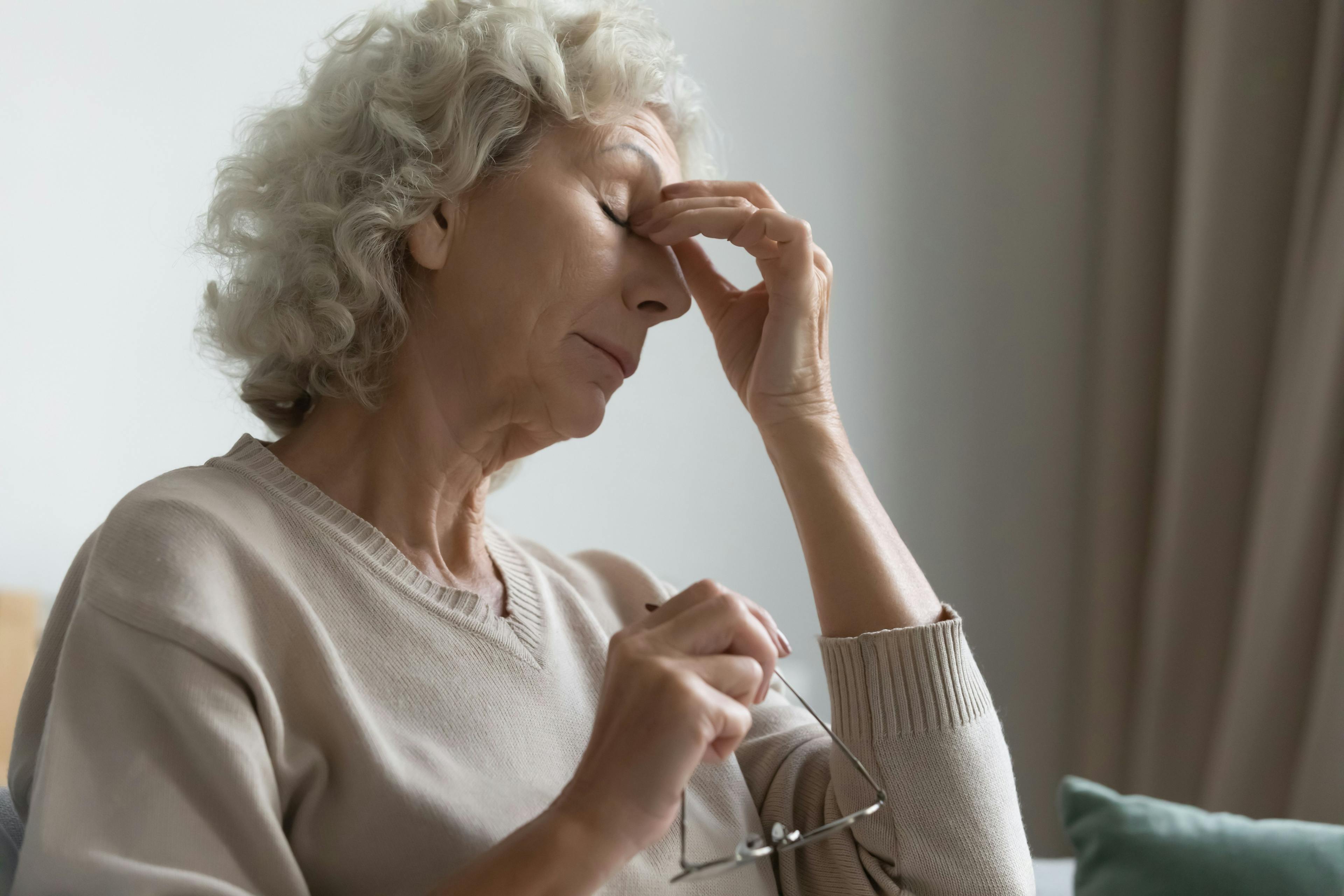 tired mature woman holding glasses and pinching bridge of her nose