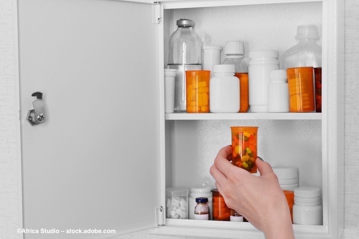 A hand reaches into a medicine cabinet to retrieve an orange bottle of pills. Image credit: ©Africa Studio – stock.adobe.com
