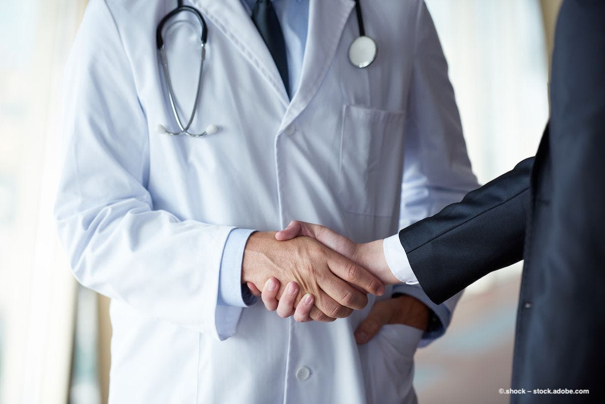 A person in a lab coat shakes hands with someone in a professional suit. Image credit: ©.shock – stock.adobe.com