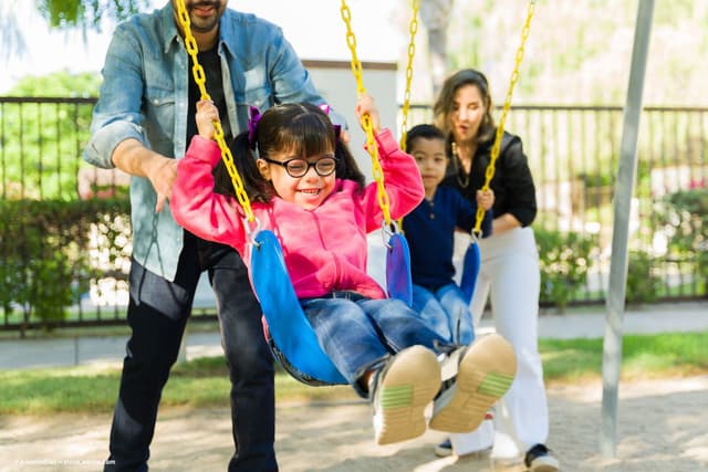 Children, one with glasses one without, are being pushed on the swings by their parents. Image credit: ©AntonioDiaz – stock.adobe.com