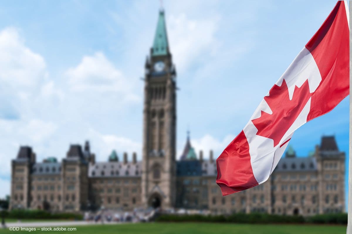 The Canadian Parliament building, with a Canadian flag waving in the foreground. Image credit: ©DD Images – stock.adobe.com