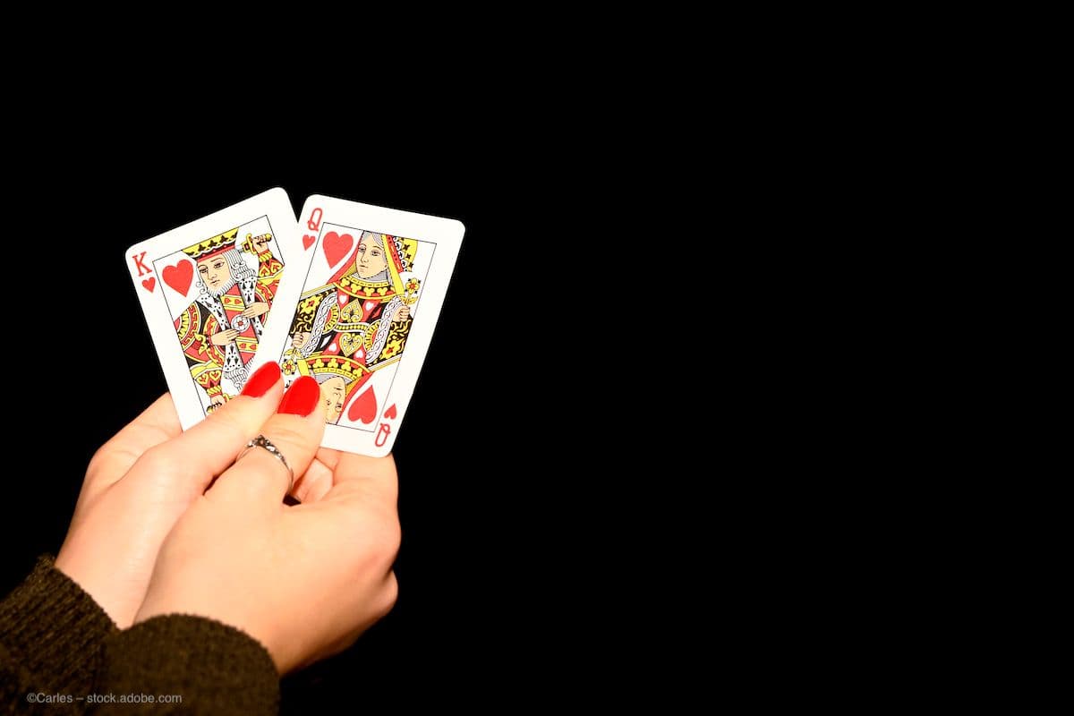 A person with painted nails holds two cards, the king and queen of hearts, against a plain black background. Image credit: ©Carles – stock.adobe.com