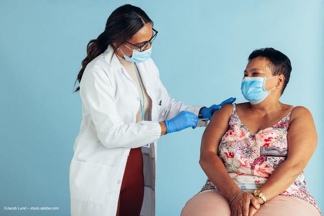 A clinician administers a COVID-19 vaccine to a patient. Both wear masks. Image credit: ©Jacob Lund – stock.adobe.com