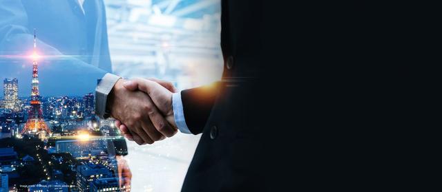 Two business professionals shake hands with a cityscape in the background