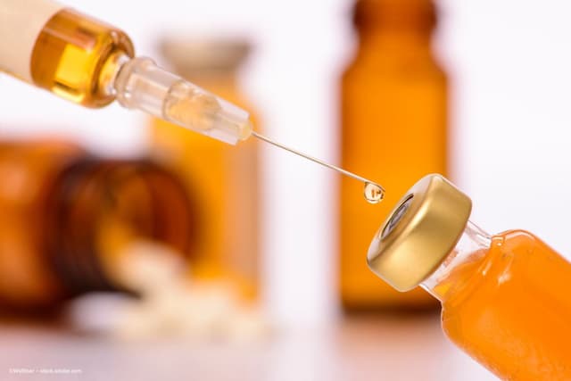 A syringe pulls from a vial of orange liquid. Image credit: ©Wolfilser – stock.adobe.com