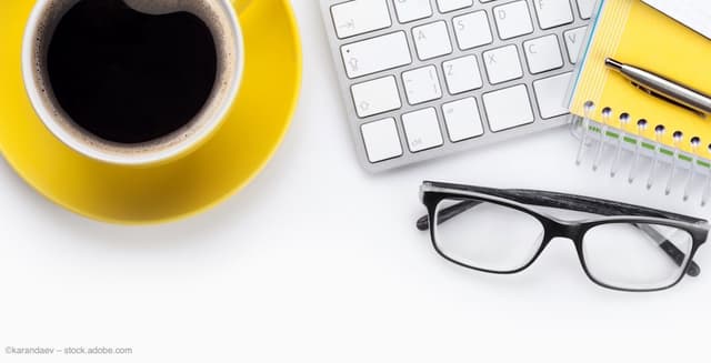 A cup of coffee and a pair of glasses sit on a desk, alongside a keyboard and notebook. Image credit: ©karandaev – stock.adobe.com