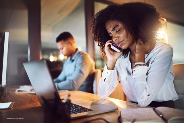 A woman with curly hair frowns, sitting at her computer in low light. Image credit: ©peopleimages.com – stock.adobe.com