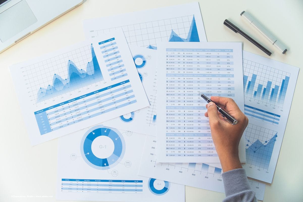 A hand reaches out and, using a pen, adds or changes data on charts. Image credit: ©Chaosamran_Studio – stock.adobe.com