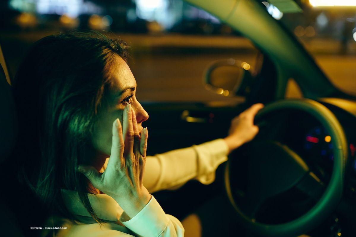 A woman driving at night touches her eye. Image credit: ©Drazen – stock.adobe.com