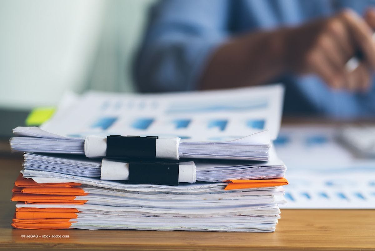 A pile of papers bound together with binder clips sits on a desk. Image credit: ©PaeGAG – stock.adobe.com