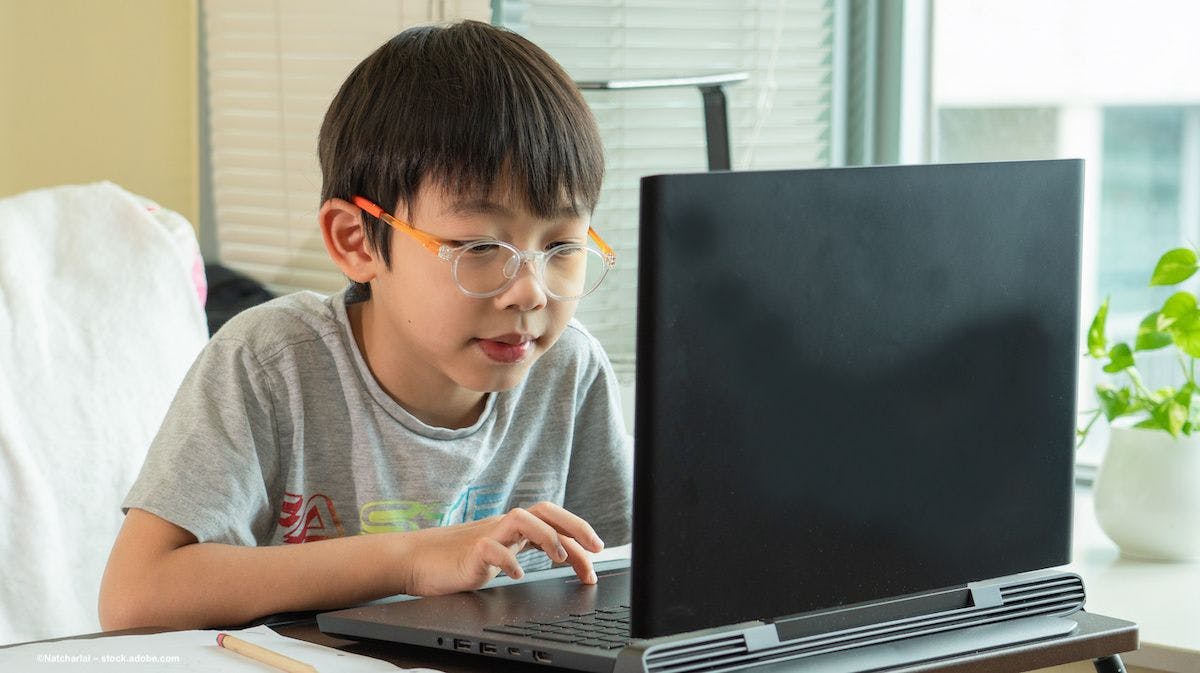 A child wearing glasses uses a laptop computer. Image credit: ©Natcharlai – stock.adobe.com