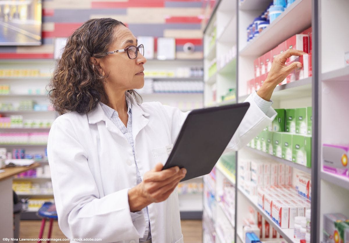A pharmacist wearing glasses reaches up to take prescriptions from a shelf. Image credit: Nina Lawrenson/peopleimages.com – stock.adobe.com