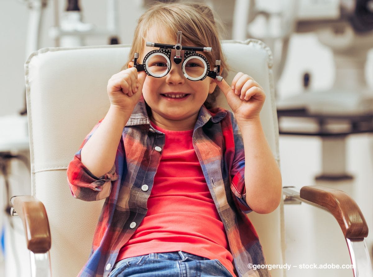 A smiling child sits in a chair, preparing to undergo an eye exam. Image credit: ©georgerudy – stock.adobe.com