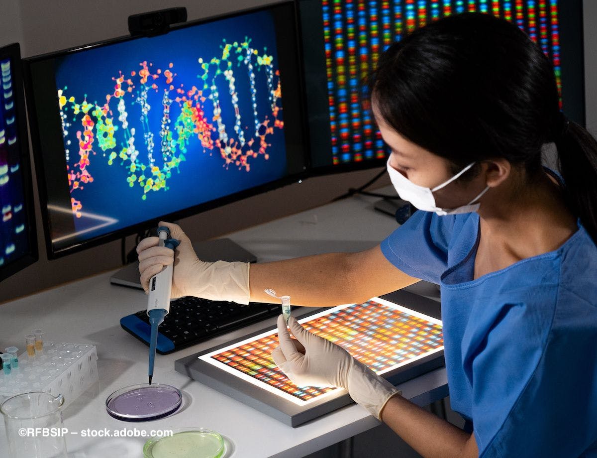 A scientist working at a computer station in a lab, where a gene is mapped on the screen behind her. Image credit: ©RFBSIP – stock.adobe.com