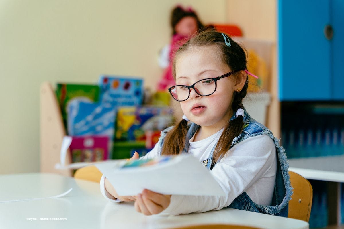 A young girl with glasses sits in a classroom, cutting paper. Image credit: ©Iryna – stock.adobe.com