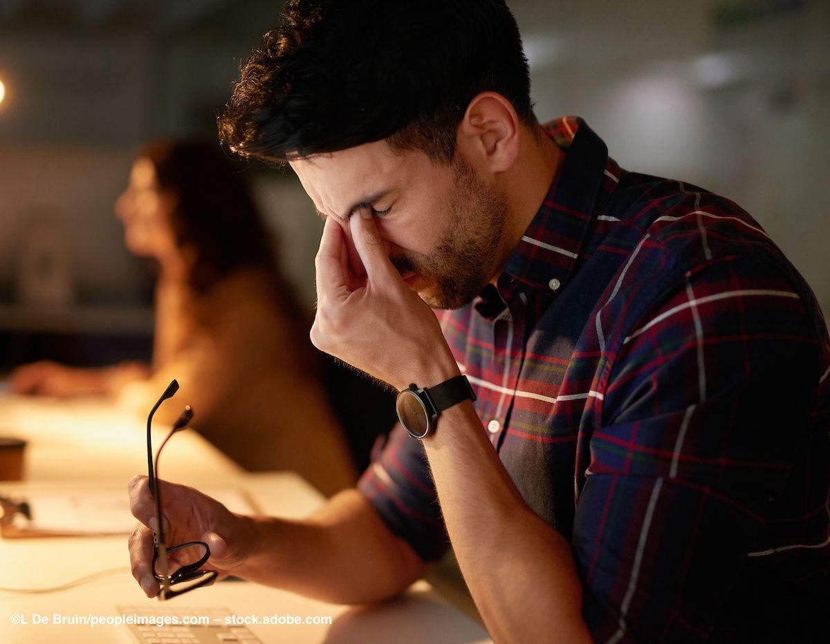 A man rubs his eyes in pain while sitting at a computer. Image credit: ©L De Bruin/peopleimages.com – stock.adobe.com