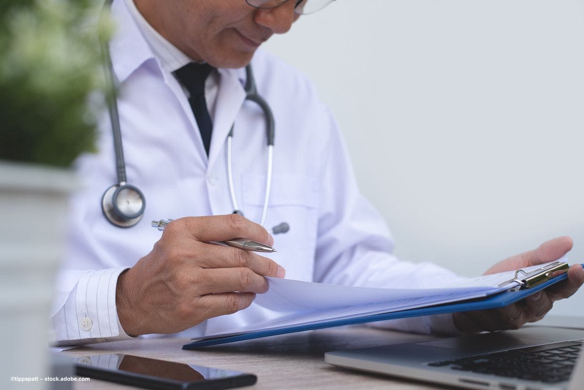 A physician consults a patient's chart on a clipboard. Image credit: ©tippapatt – stock.adobe.com