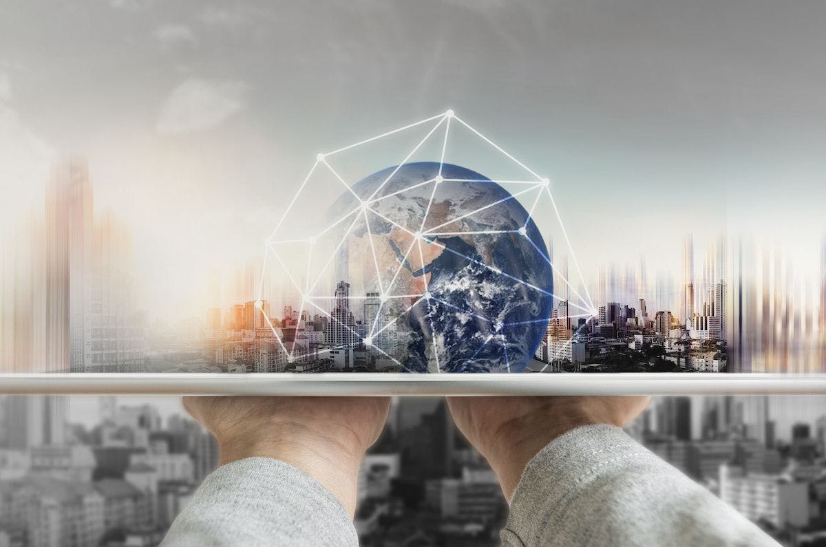 A digital rendering of the globe sits on a tray, lifted by a pair of anonymous hands. A cityscape is blurry in the background. Image credit: ©SasinParaksa – stock.adobe.com