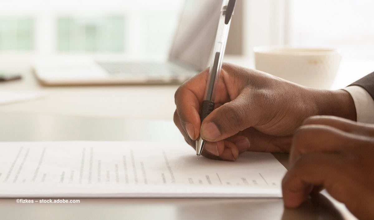 A hand signs a contract on a table. Image credit: ©fizkes – stock.adobe.com